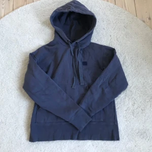 Blå hoodie från Acne Studios - Säljer en stilren grå hoodie från Acne Studios med en klassisk känguruficka och justerbar huva. Tröjan har en diskret logotyp på bröstet, ny pris på såna här hoodies är runt 1700-2200kr, hör av er vid frågor