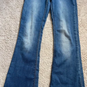 Blå bootcut jeans från LMTD - Säljer ett par klassiska blå bootcut jeans från LMTD. Jeansen har lätt slitna partier framtill och två bakfickor. Perfekta för dig som gillar en retroinspirerad look med utsvängda ben.