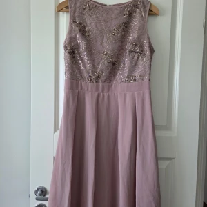 Klänning - Elegant ljuslila långklänning med vacker broderad och glittrig överdel. Klänningen har ärmlös design och rund halsringning
