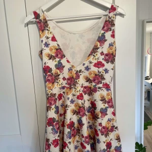 Blommig klänning från Sisters Point - Superfin blommig klänning från Sisters Point med v-ringning och ärmlös design. Klänningen har en vit bas med färgglada blommor i rött, gult och lila. Perfekt för sommarens alla tillfällen! Storlek S💗 Använd inte köp nu!