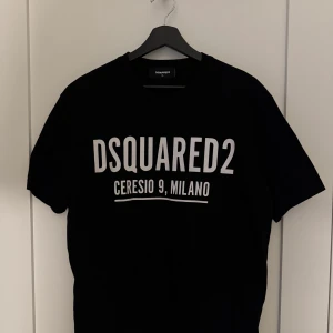 Svart t-shirt från Dsquared2 - Snygg svart t-shirt från Dsquared2 med vit text 'DSQUARED2 CERESIO 9, MILANO' på bröstet. Klassisk passform och rund halsringning. Perfekt för en stilren och trendig look. Passar medium & large