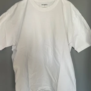 Vit t-shirt från New Gamers - Säljer en stilren vit t-shirt från New Gamers med ett diskret broderat smiley-ansikte på bröstet. Perfekt för en avslappnad look. T-shirten har en normal passform och är kortärmad. Passar till alla tillfällen!