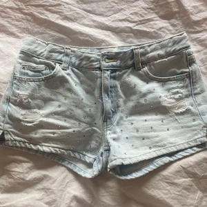Ljusblå jeansshorts - Snygga ljusblå jeansshorts med slitna detaljer och ”rhinestones”. Några stenar har ramlat av men det syns inte när man har på sig 