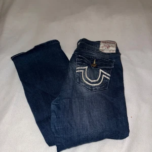 Blå jeans från True Religion - Snygga blå jeans från True Religion med bootcut-stil och dekorativa sömmar på bakfickorna. De har en medelhög midja och klassisk femficksdesign. Perfekta för en avslappnad look.