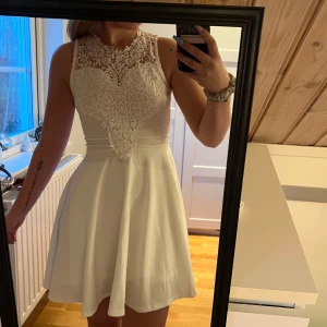 Vit spetsklänning med öppen rygg - Säljer en elegant vit klänning med spetsdetaljer och en vacker öppen rygg. Perfekt för sommaren studenten eller en avslutning. Klänningen är ärmlös och har en kort längd som passar perfekt för sommarens fester. Den har en dragkedja i ryggen för enkel påklädning💞