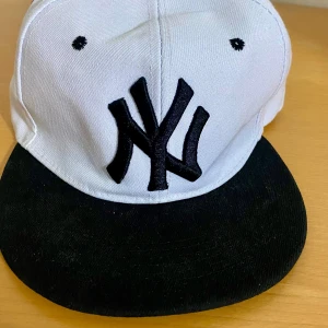 Vit och svart keps med broderad logga - Snygg keps i vitt med svart skärm och broderad logga framtill. Justerbar passform med snapback-stängning. Perfekt för en casual look. Passar alla och kan vara fin på en sommar dag, passar med alla kläder typ