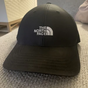 Svart keps från The North Face - Snygg svart keps från The North Face med broderad logga framtill. Justerbar rem baktill för perfekt passform. Perfekt för både vardag och äventyr.      
