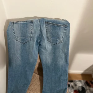 Blå jeans med slitningar - Snygga blå jeans med slitningar på framsidan. De har en klassisk femficksdesign och en dragkedja. Perfekta för en avslappnad stil.