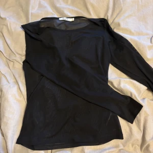 Svart långärmad topp från NA-KD - Säljer en stilren svart långärmad topp från NA-KD. Perfekt för en elegant och minimalistisk look. Toppen har en enkel design med rund hals och är tillverkad i ett lätt material.