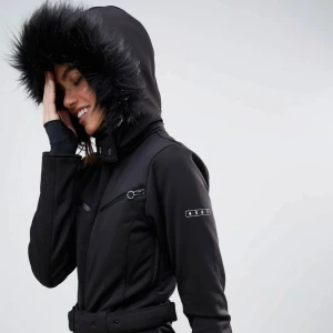 Svart overall med pälsdetaljer från ASOS 4505 - Snygg svart overall från ASOS 4505 i storlek 34 med pälsdetaljer på huvan. Den har dragkedja framtill och justerbart bälte i midjan för en perfekt passform. Perfekt för vinterns äventyr i snön! ❄️köpte den nyss men storleken  passade inte så säljer den vidare. 🎿