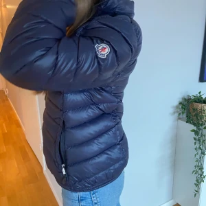 Marinblå jacka från Moncler - Säljer en snygg marinblå jacka från Moncler då jag inte har så mycket användning för den. Jackan är i bra skick och passar mig som vanligtvis har XXS/XS i storlek. Jag på bilden är 157cm lång. Det finns även en luva man kan veckla ut på jackan. Jag har inget äktehetsbevis.