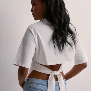 Vit croppad open back tie Nelly  - Säljer en stilren vit croppad topp med korta ärmar och knytning i ryggen ifrån Nelly 