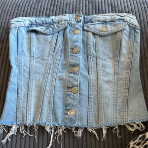 Jeans topp från Zara - Säljer en cool jeans topp från Zara med knappar framtill och fransig nederkant. Toppen har en smockdetalj baktill för extra stretch och passform. Perfekt för en avslappnad look!