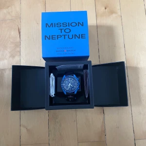 Omega x swatch  - Säljer en snygg blå klocka från Swatch x Omega, Mission to Neptune. Klockan har en blå urtavla med vita detaljer och en svart rem. Perfekt för den som gillar en sportig och modern stil. Allt og följer med. Tveka inte på att skriva vid minsta fundering och ifall fler bilder önskas.
