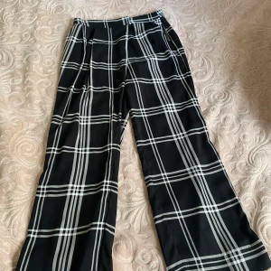 Svarta rutiga byxor med dragkedja - Snygga svarta byxor med vitt rutmönster. De har en dragkedja på sidan och en stilren design. Super sköna och luftiga med tunnt material 💞priset går att diskutera💗köpte på Lindex.