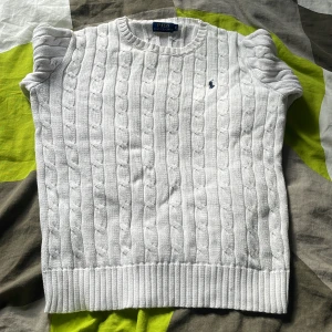 Vit stickad tröja från Ralph Lauren - Säljer en stilren vit stickad tröja från Ralph Lauren med kabelstickat mönster. Tröjan har långa ärmar och en klassisk rund halsringning. Perfekt för en elegant och avslappnad look.