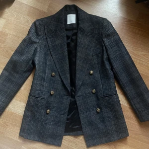 Grå/blå rutig kavaj med guldknappar från Sandro Paris - Snygg grå rutig kavaj från Sandro Paris med dubbelknäppning och stiliga guldknappar. Perfekt för en classic look. Formen är super snygg och är i mycket bra skick.