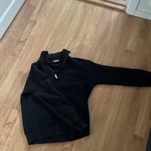 Svart ribbad tröja från Kappahl - Säljer en svart ribbad tröja från Kappahl med dragkedja vid halsen. Tröjan har långa ärmar och en hög krage, perfekt för kyligare dagar. Den är både stilren och bekväm, ett måste i garderoben! Knappt använd och bra i skick!