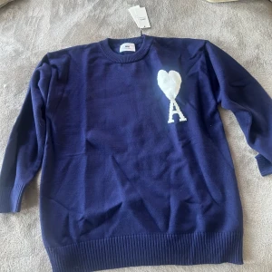 Mörkblå tröja från Ami - Säljer en snygg mörkblå tröja från Ami med ett vitt hjärta och bokstaven 'A' på bröstet. Tröjan har långa ärmar och en ribbad krage samt nederkant. Perfekt för en stilren look. Helt oanvänd då den är för stor för min son. Köpt i Paris, därav kan vi inte byta storlek. Så ny med prislapp på, självklart äkta! Dyr i inköp!