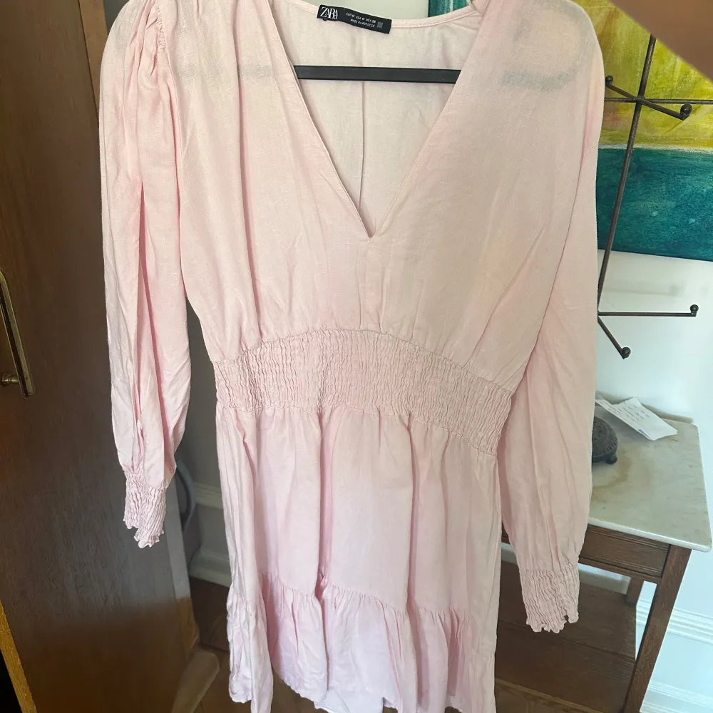 Säljer en söt ljusrosa klänning från Zara med v-ringning och långa ärmar. Klänningen har smockdetaljer i midjan och vid ärmsluten, vilket ger en fin passform. Perfekt för vår och sommar!. Mekot.
