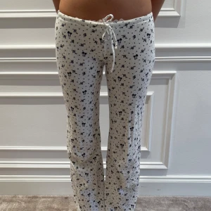 Vit mjukisbyxa med blommönster från Nelly - Säljer ett par vita mjukisbyxor från Nelly med ett sött blommönster i svart. Byxorna har en bekväm passform med snörning i midjan för justerbarhet. Perfekta för en avslappnad dag hemma.