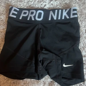 Svarta träningsshorts från Nike - Snygga svarta träningsshorts från Nike med en elastisk midja och vit logga. Perfekta för gymmet eller löprundan. Bekväma och stilrena med en tight passform.