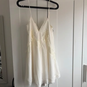 Vit klänning  - Söt vit klänning från Pull&Bear med smala axelband och spetsdetaljer. Klänningen har en v-ringad design och är perfekt för varma dagar. Den är tillverkad i ett lätt och luftigt material som ger en bekväm passform.