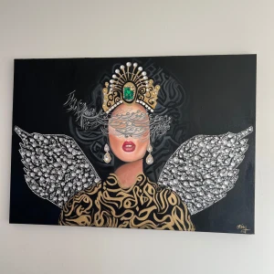 Målning med kvinna i krona och vingar - En konstnärlig målning av en kvinna med en krona dekorerad med pärlor och en stor grön sten. Hon har stora örhängen och vingar av glittrande stenar. Bakgrunden är svart och klänningen har ett guldmönster.