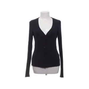 Svart ribbad kofta från Weekday - Snygg svart kofta från Weekday med ribbad struktur och v-ringning. Den har långa ärmar och knappar framtill, perfekt för en stilren look. Passar bra till både jeans och kjol. Storlek M