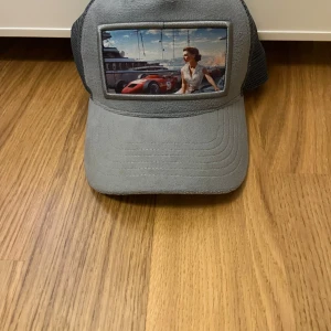 Blå velvet keps med bil på  - Snygg blå keps med ett coolt bilmotiv på framsidan. Kepsen har ett nätmaterial på baksidan för bättre ventilation och en böjd skärm. Perfekt för bilentusiaster eller som en stilren accessoar.