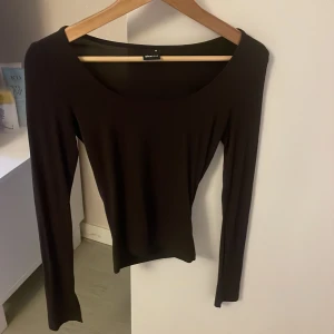 Mörkbrun långärmad topp från Gina Tricot - Säljer en stilren långärmad topp från Gina Tricot. Väldig soft material och sluta vid bögge armarna. Använd 1 gång endast  