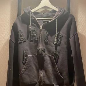 Mörkblå Zip Hoodie från Axel Arigato - Säljer en mörkblå zip hoodie från Axel Arigato med dragkedja och stor ficka framtill. Hoodien har stora bokstäver på bröstet och en justerbar huva med snören. Tillverkad i 100% ekologisk bomull, perfekt för en stilren och bekväm look. Passar både kvinnor och män, det står storlek S men passar M också! Lite oversized, riktigt snygg! Säljer för den har blivit för liten för mig, tyvärr. Köpt för: 2199kr. Priset är diskuterbart, öppen för alla frågor!😁