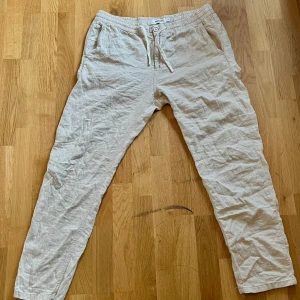 Beige linnebyxor från Kappahl - Säljer ett par bekväma beige linnebyxor från Kappahl. Byxorna har en elastisk midja med snörning och knappdetaljer framtill. Perfekta för en avslappnad stil.