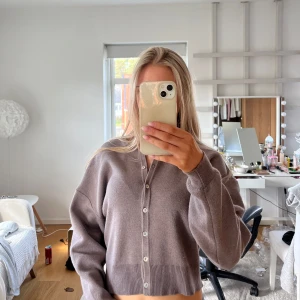 Grå kofta med knappar - Säljer en stilren brun/grå kofta med knappar framtill. Koftan har en croppad passform och långa ärmar.