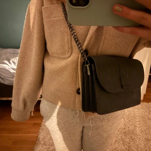 Svart axelväska med kedja - Snygg svart axelväska med en stilren design och kedja som axelrem. Väskan har en enkel flikstängning och är perfekt för att bära dina dagliga nödvändigheter. Den är både praktisk och trendig.