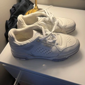 Vita sneakers från Axel Arigato - Säljer ett par stilrena vita sneakers från Axel Arigato. Skorna har en klassisk design med snörning och perforerade detaljer på sidorna. Perfekta för en avslappnad och trendig look.