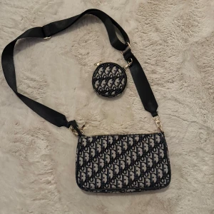 Mönstrad axelväska med rund plånbok - Snygg axelväska med matchande rund plånbok. Väskan har ett mönster i svart och beige med en justerbar axelrem i svart. Perfekt för att bära dina till alla outfits 