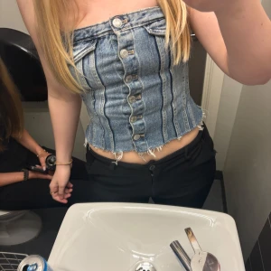 Jeanskorsett med knappar - Snygg jeanskorsett med knappar framtill och fransiga kanter. Perfekt för en trendig look. Den har en tight passform och är ärmlös, vilket gör den idealisk för varmare dagar.