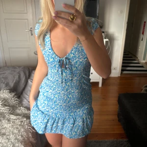 Blå blommig klänning - Söt blå klänning med blommigt mönster och volangdetalj. Perfekt nu till sommaren!!