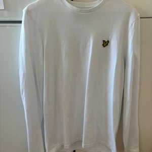 Vit långärmad tröja från Lyle & Scott - Säljer en NY stilren vit långärmad tröja från Lyle & Scott med deras ikoniska logga på bröstet. Perfekt för en avslappnad och snygg look. Tröjan är i mjukt material och har en normal passform. 