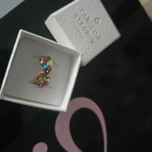 Caroline Svedbom stella ring  - Säljer en fantastisk ring från Caroline Svedbom modell stella, rainbow combo stenar och guld ring. Endast använda vid ett par tillfällen. Nypris 900kr