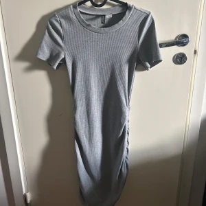 Grå ribbad klänning från H&M Divided - Snygg grå ribbad klänning från H&M Divided i storlek XS. Klänningen har korta ärmar och en stilren design med rynkade detaljer på sidan. Perfekt för en avslappnad look.