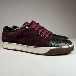 Lanvins 44 sällsynta - Snygga vinröda sneakers från Lanvin med unika ormskinnsdetaljer på tå och häl. Skorna har en vit sula och matchande vinröda snören som ger en cool kontrast. Perfekta för dig som vill sticka ut med stil. Skit sällsynta lanvins i storlek 44 bara skorna följer med 