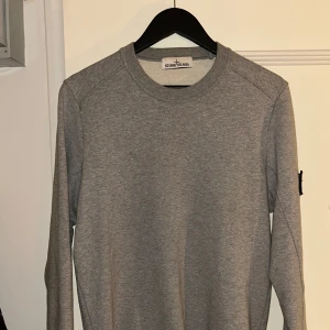 Stone Island Sweatshirt Grey M - Säljer en stilren grå långärmad tröja från Stone Island. Tröjan har en klassisk design med rund hals och det ikoniska Stone Island-märket på ärmen. Inga defekter eller märken. Nypris: 2999kr Storlek: Medium. Passar mig som är 183cm.