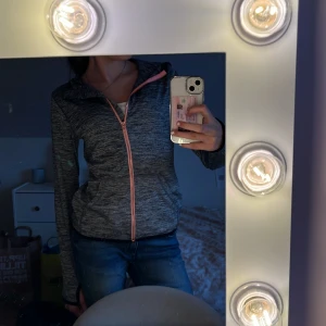 Grå zip up från H&M Sport - Säljer en grå zip up från H&M Sport med dragkedja och rosa detaljer. Perfekt för träning eller en avslappnad dag. 💕Den har långa ärmar och en bekväm passform. Hör av dig vid intresse!
