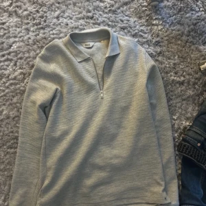 Grå långärmad tröja med dragkedja - Säljer en stilren grå långärmad tröja med dragkedja vid halsen. Tröjan har en klassisk krage och är perfekt för en avslappnad look. Den är i en mjuk och bekväm kvalitet. Har inga defekter och är som helt ny 