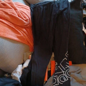 Svarta träningsbyxor från Adidas - Säljer ett par svarta träningsbyxor från Adidas med vit logga längs benet. Byxorna har en bekväm passform och är perfekta för träning eller avslappnade dagar. Tillverkade i ett mjukt och stretchigt material.