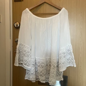 Vit blus med spetsdetaljer från Chica London - Säljer en vacker vit blus från Chica London med spetsdetaljer på ärmar och nederkant. Blusen har en offshoulder-design och är tillverkad i 100% viskos. Perfekt för en somrig look!