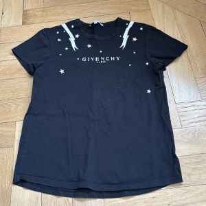 Svart t-shirt med stjärnor från Givenchy - Snygg svart t-shirt från Givenchy med vita stjärnor och banddetaljer. Perfekt för en stilren look med en touch av lyx. Givenchy-loggan pryder framsidan. Det är storlek +14 men passar mig som har xs.