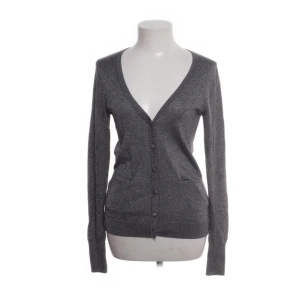 Grå kofta från Vila - Snygg grå kofta från Vila med v-ringning och knappar framtill. Koftan har långa ärmar och man ser lite glitter i ljuset!